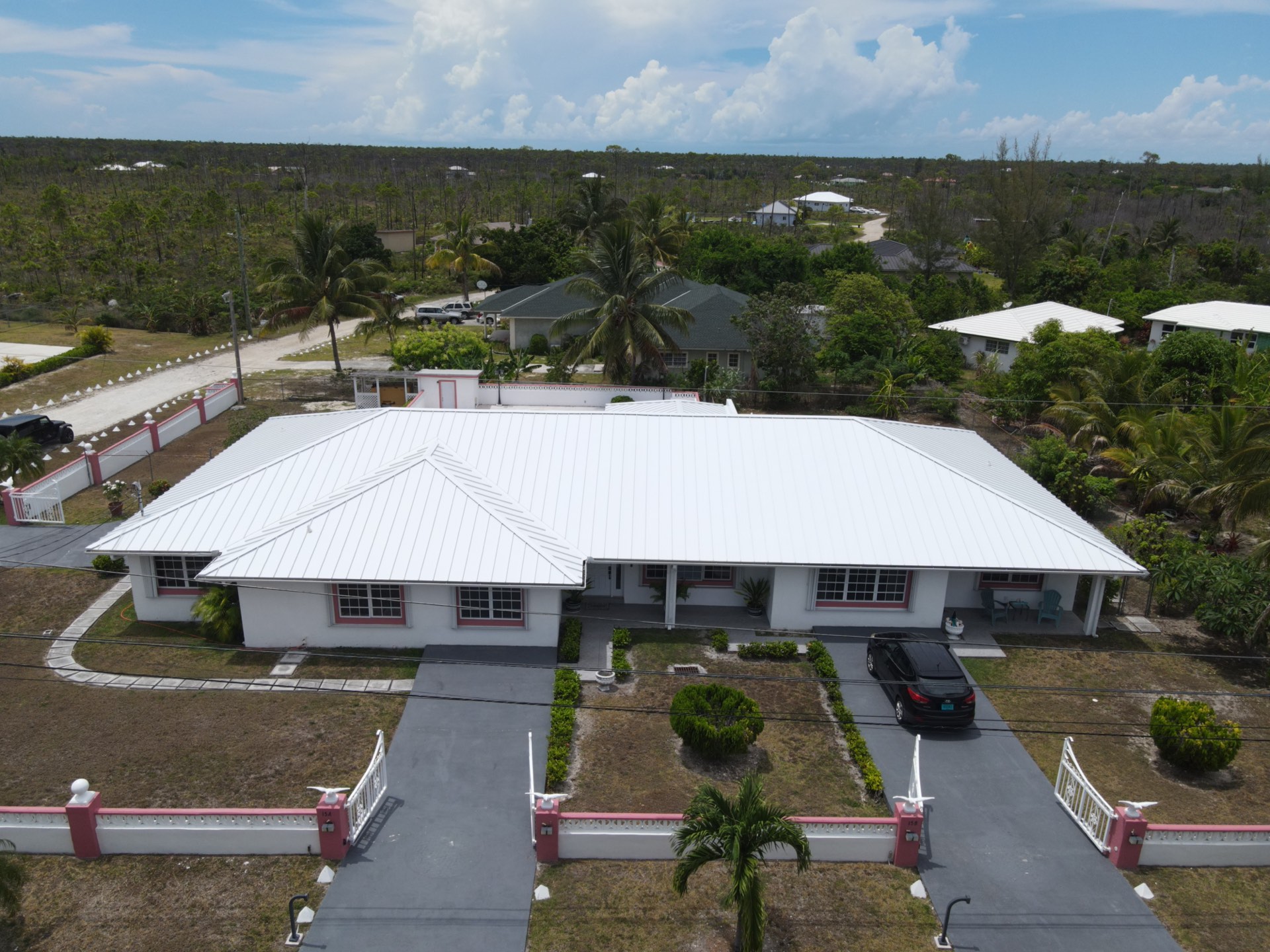 White metal-roof custom home with pool and gated red-trimmed perimeter wall, Grand Bahama